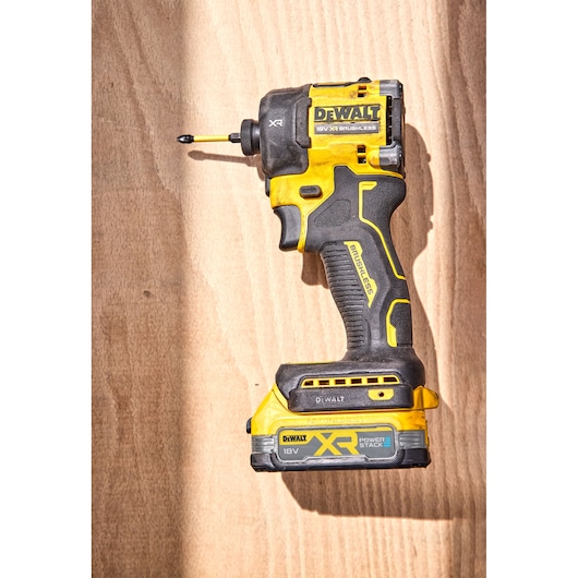 A DEWALT 18V XR brushless cordless impact driver with POWERSTACK battery, shown on a wooden surface.