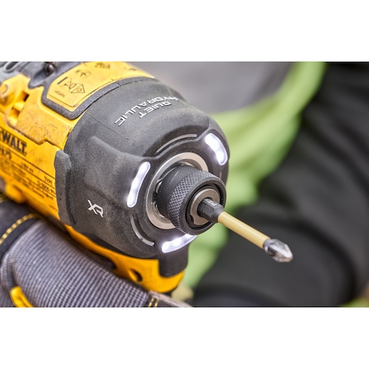 Close-up view of a DEWALT cordless impact driver, showing its illuminated front, the XR mark, and a mounted screwdriver bit. The tool is held by a gloved hand.