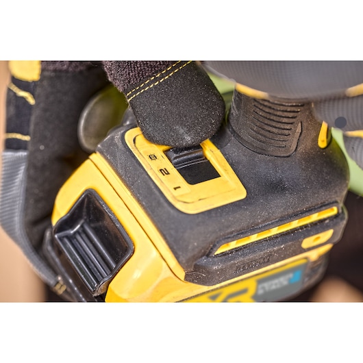 Close-up of a gloved hand adjusting the setting switch on a DEWALT power tool, showing the yellow and black design with visible numbers and textured grip.