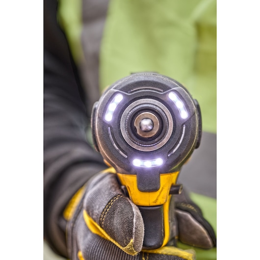 Close-up view of a DEWALT power tool, specifically showing the front of an impact wrench with LED lights illuminated, being held by a person wearing protective work gloves.