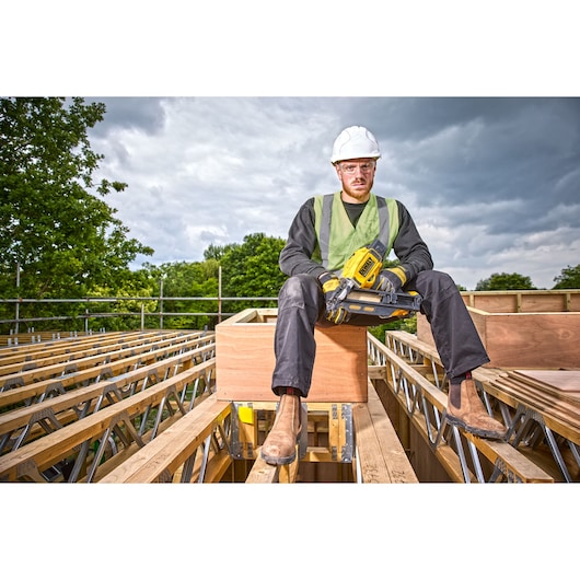	Construction worker sitting on top of a rooftop holding a DCN930 18V XR Brushless framing nailer 