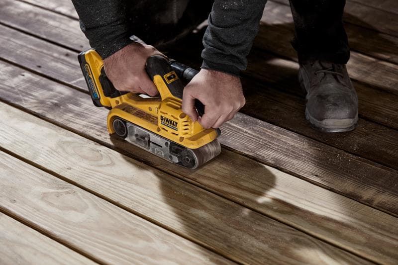 A person using a yellow DEWALT cordless belt sander on wooden boards to smooth their surface.