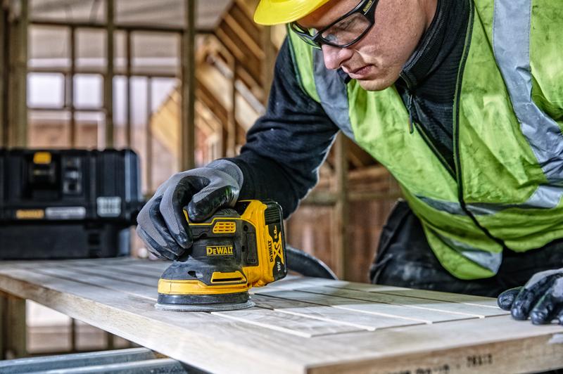 DEWALT DCW210, DCW210D1 sander in use on wood in construction scene. Person is wearing gloves and safety vest.